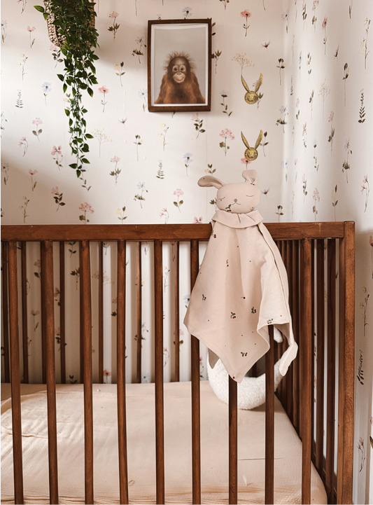 Wooden crib with a baby blanket hanging over the side in a room with floral wallpaper.